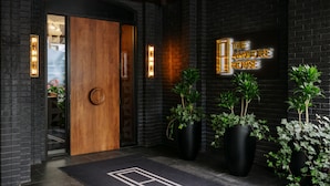 Une entrée moderne avec une porte en bois, des murs en briques noires et de grandes plantes en pot.