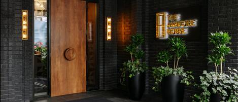 A modern entrance with a wooden door, black brick walls, and large potted plants.