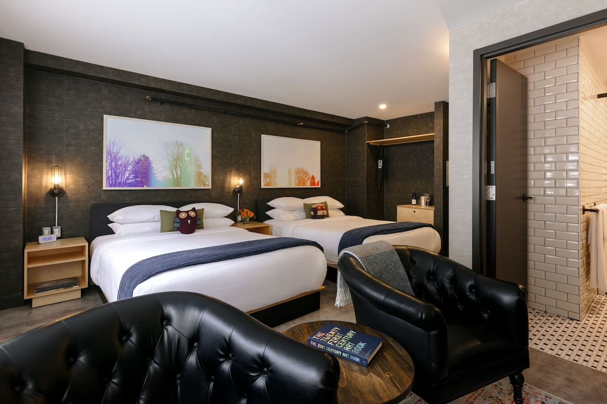 Une chambre d’hôtel moderne avec deux lits, un coin salon comprenant un fauteuil en cuir, une petite table avec un livre, et des œuvres d’art accrochées aux murs.
