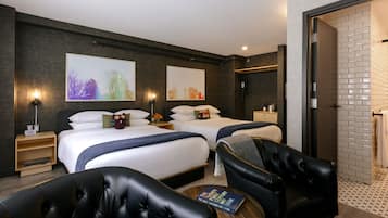 Une chambre d’hôtel moderne avec deux lits, un coin salon comprenant un fauteuil en cuir, une petite table avec un livre, et des œuvres d’art accrochées aux murs.