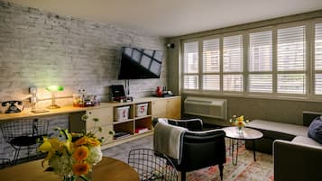 A modern living room with a brick wall, a flat-screen TV, a wooden dining table, and a sofa.