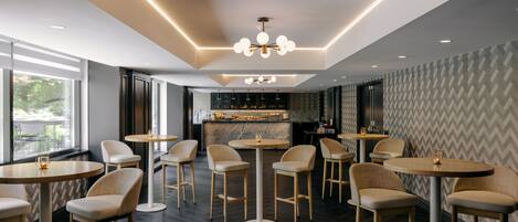 A modern bar area with round tables and bar stools, a marble countertop, and a patterned wall.