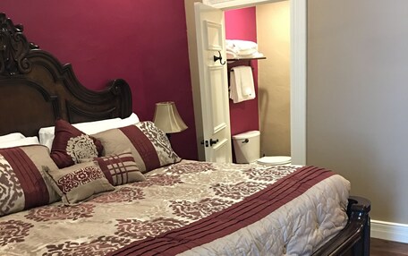 A bedroom with a wooden bed, a nightstand, a lamp, and a door leading to a bathroom.