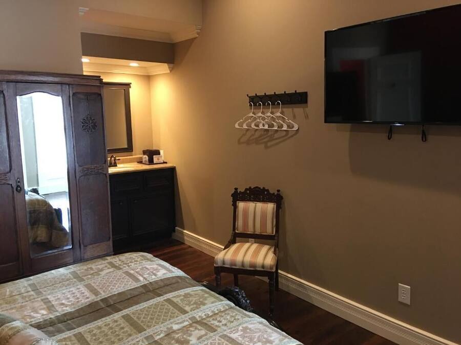 A bedroom with a bed, a dresser, a chair, a TV, and a coat rack.