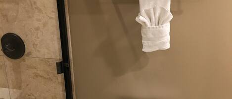 A bathroom with a toilet, a shower, and a towel rack with folded towels.