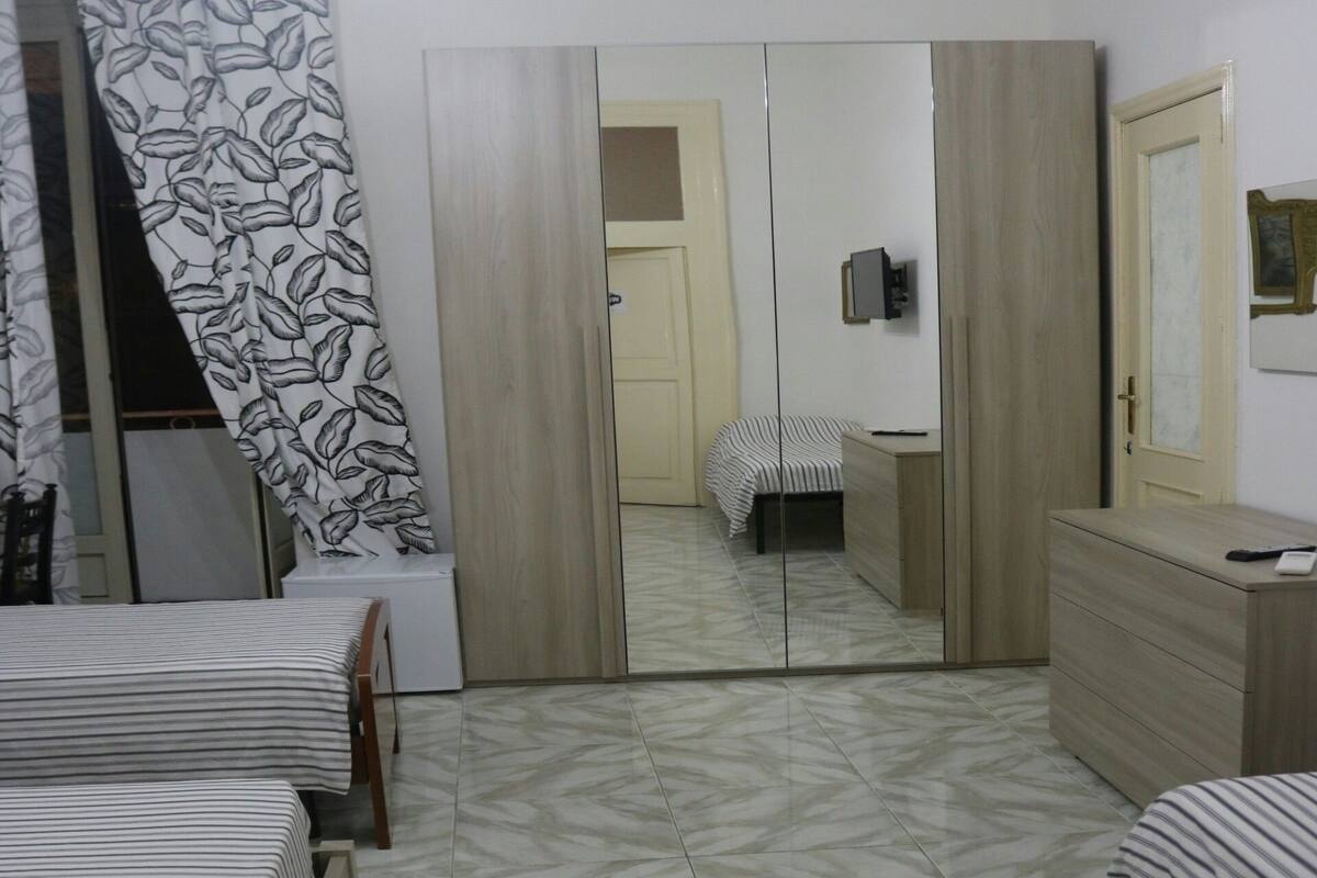 A bedroom with two beds, a wardrobe, a mirror, and an air conditioning unit.