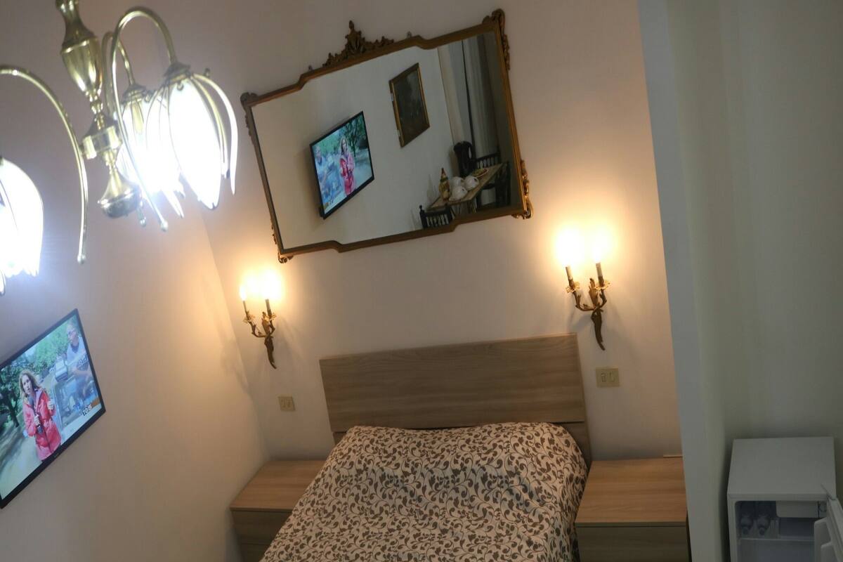 A bedroom with a bed, a nightstand, a dresser, a mirror, and wall-mounted lights.