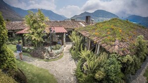 Une maison traditionnelle avec un toit recouvert de tuiles rouges, entourée d’une végétation luxuriante et bordée d’un chemin de pierre.