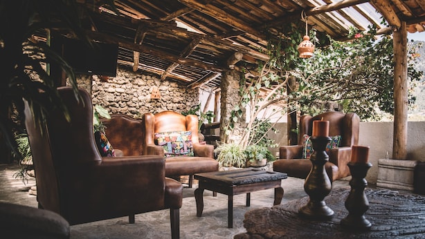 Un espace extérieur aménagé dans un style rustique, avec des canapés en cuir, une table basse en bois et un sol en pierre.