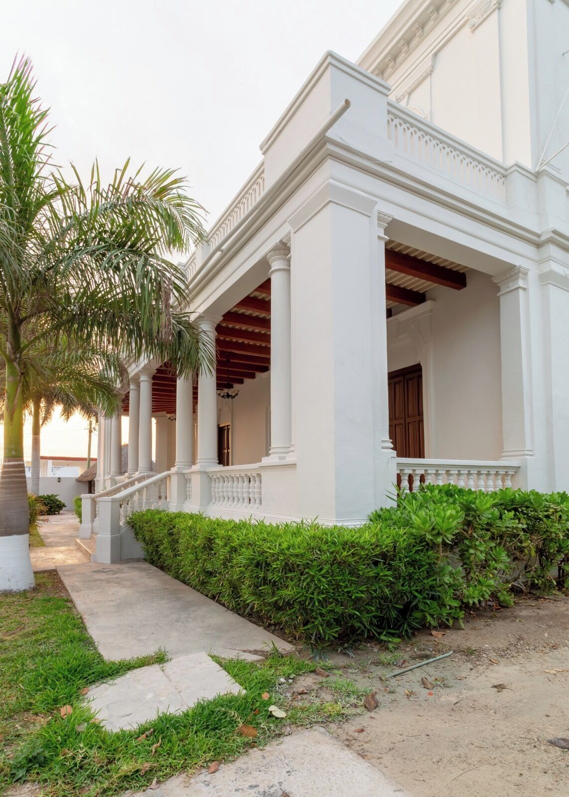 Un edificio blanco con un porche cubierto, columnas y un camino que lleva a la entrada.