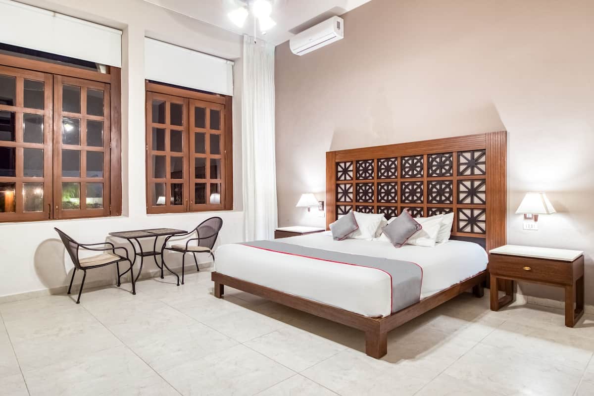 A bedroom with a bed, bedside tables, a chair, a small table, and a window with curtains.