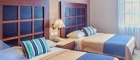 A hotel room with two beds, a nightstand, a lamp, and a window with curtains.