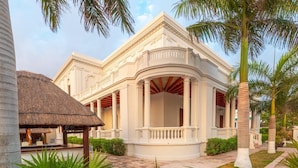 A white colonial-style building with a central courtyard, surrounded by palm trees and potted plants. - Tecnohotel Casa Villamar (Progreso)