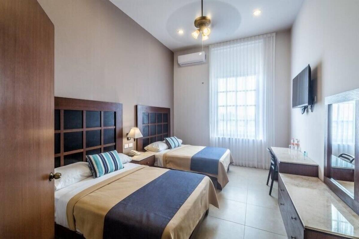 A hotel room with two beds, a desk, a chair, a television, and a window with curtains.