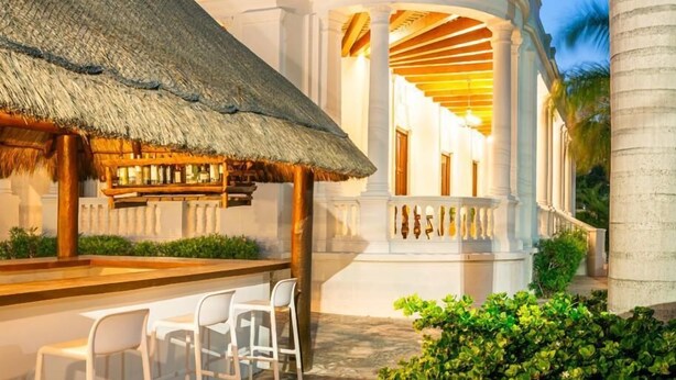 A resort with a thatched-roof bar area, white columns, and a well-maintained garden. - Tecnohotel Casa Villamar (Progreso)