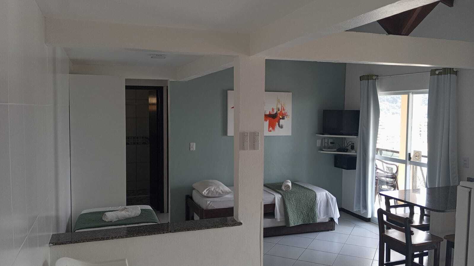 A hotel room with two beds, a dining area with a table and chairs, a TV, and a balcony with curtains.