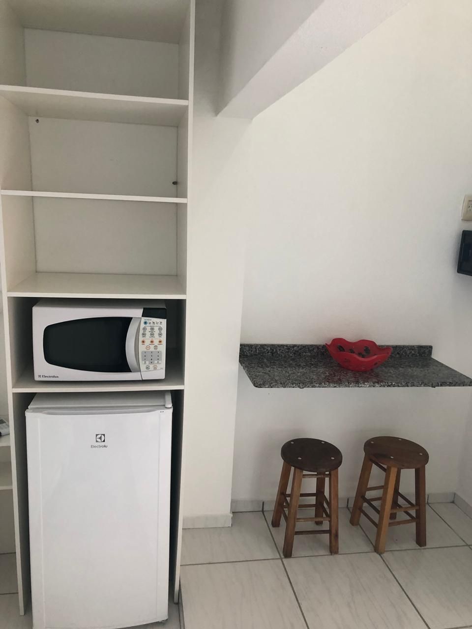 A kitchen with a microwave, a refrigerator, and two stools.