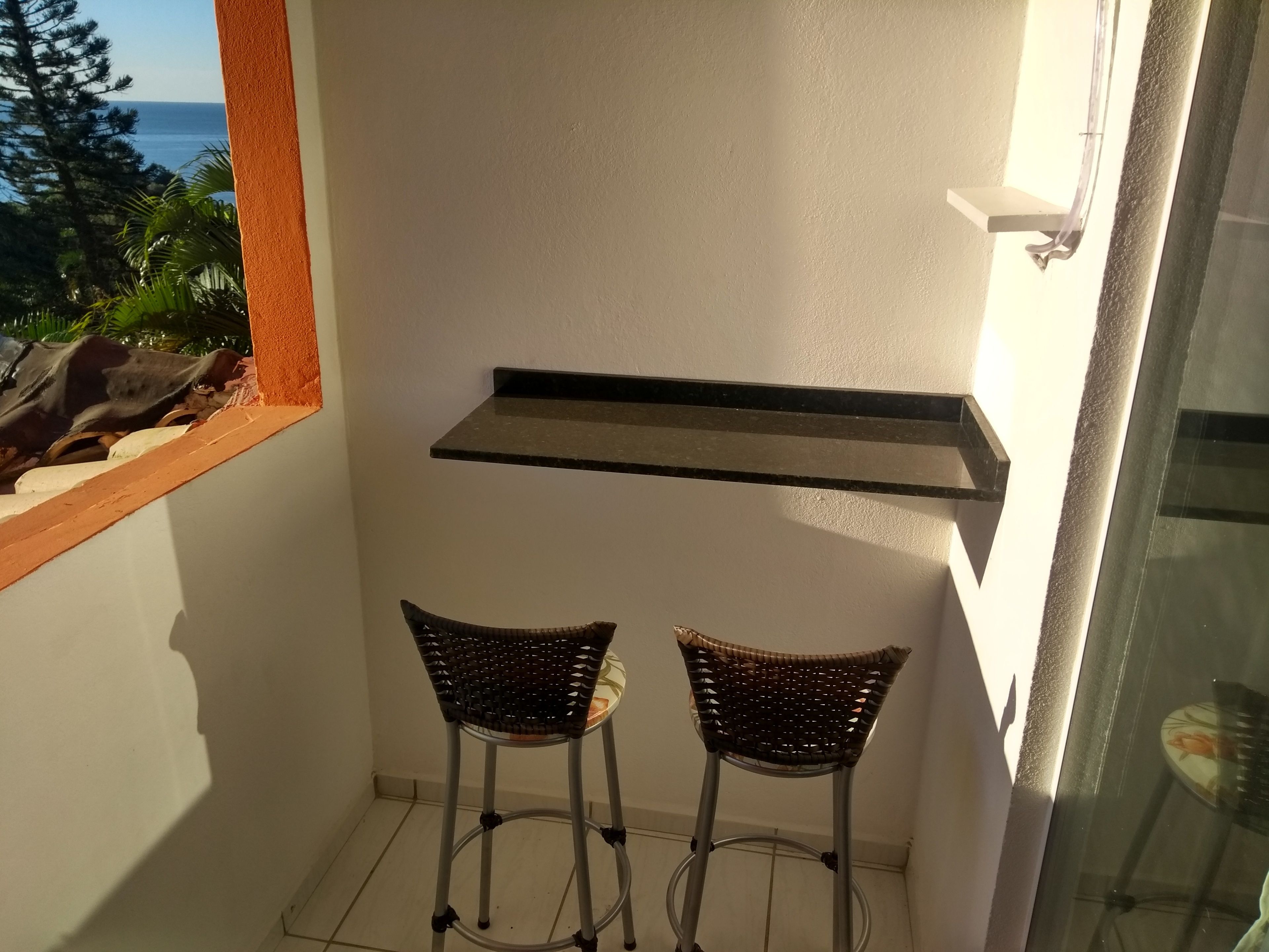 Un balcon avec deux fauteuils en osier, une petite étagère noire et une vue sur la mer.
