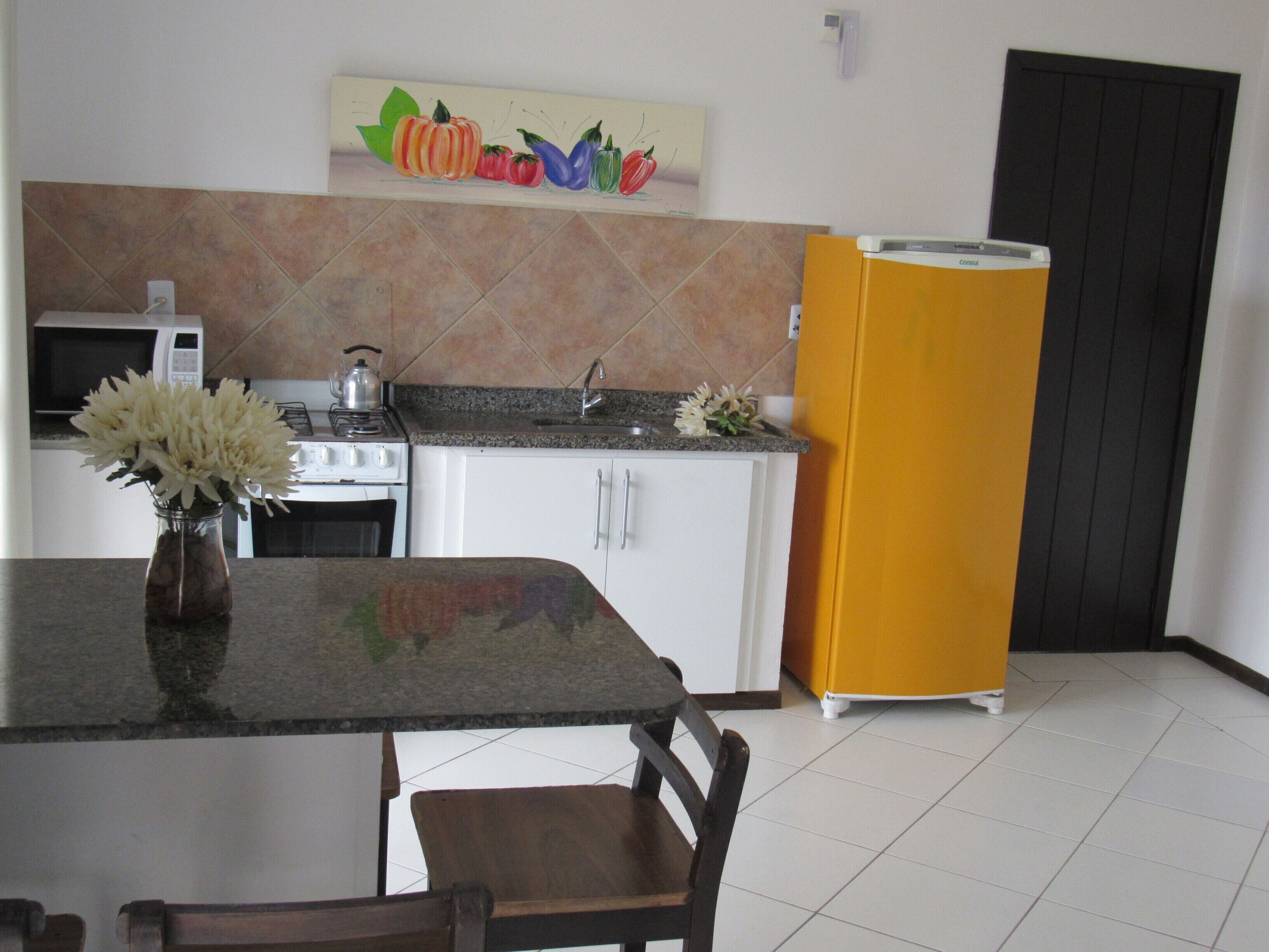 A kitchen with white cabinets, a granite countertop, a stove, a microwave, a sink, and a yellow refrigerator.