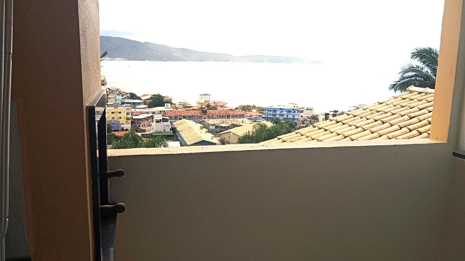 A view from a balcony overlooking a coastal town with buildings and a body of water in the distance.