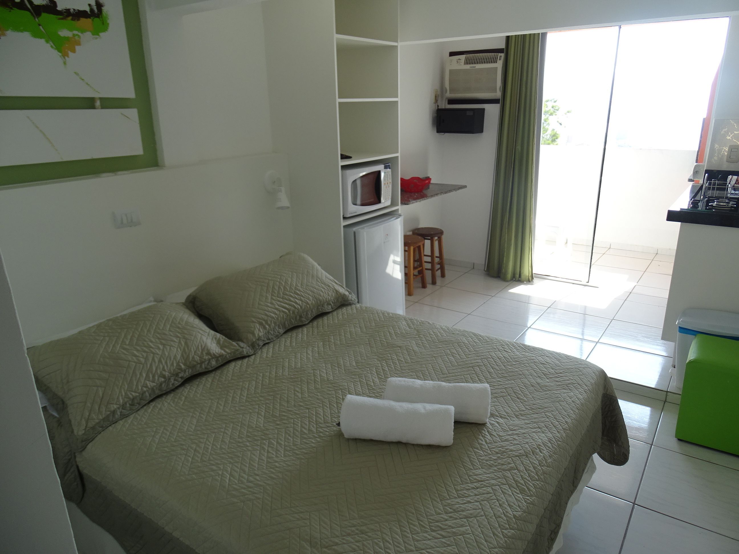 Ein Hotelzimmer mit Bett, Küchenzeile, einer kleinen Essecke und Blick durch eine Glastür.