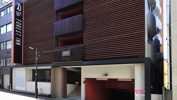 A modern building with a prominent 'R5 Forest Inn' sign, featuring a unique architectural design with slatted wooden panels and a visible staircase leading to an entrance.