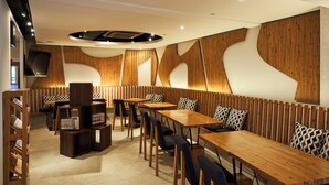 A modern restaurant with wooden panel walls, round tables, and black upholstered chairs.