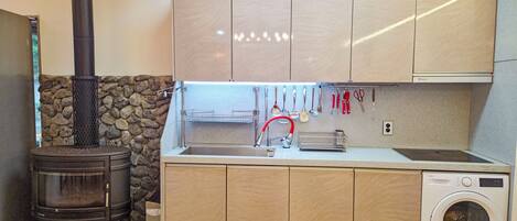 A compact kitchen with a built-in stove, a washing machine, and a stone wall.