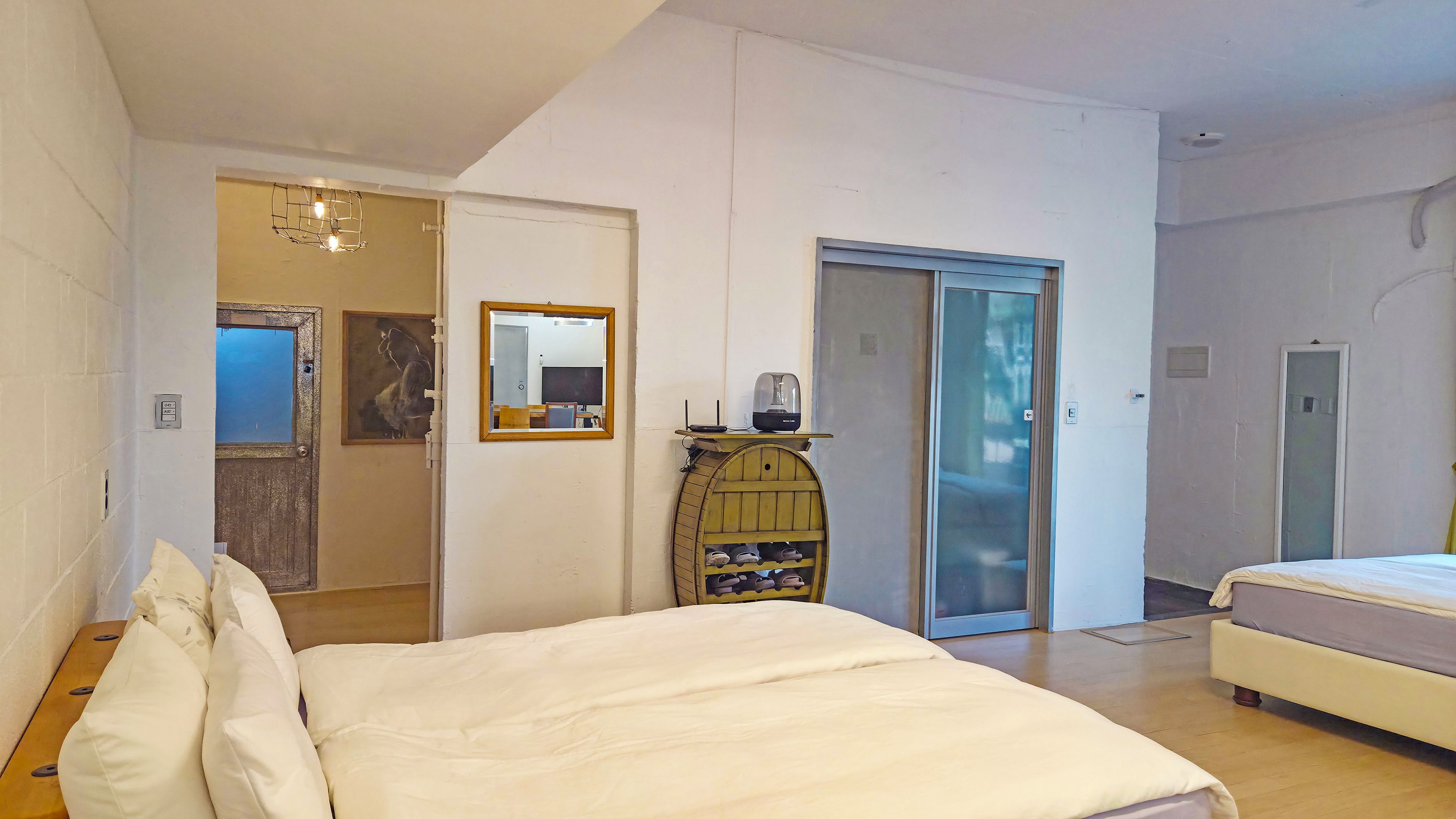 Quarto de hotel com cama, sapateira de madeira, espelho e porta para outro cômodo.