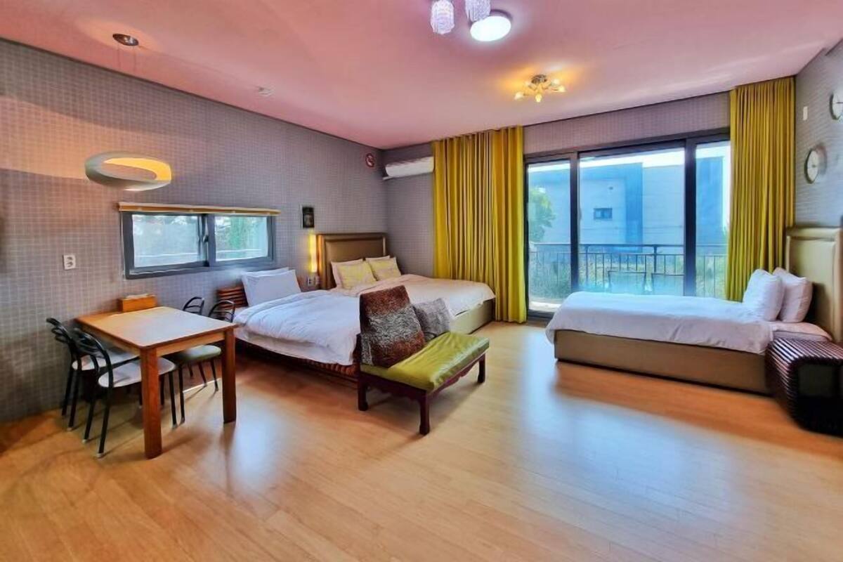 A hotel room with a bed, a desk, a chair, a bench, and a balcony with curtains.