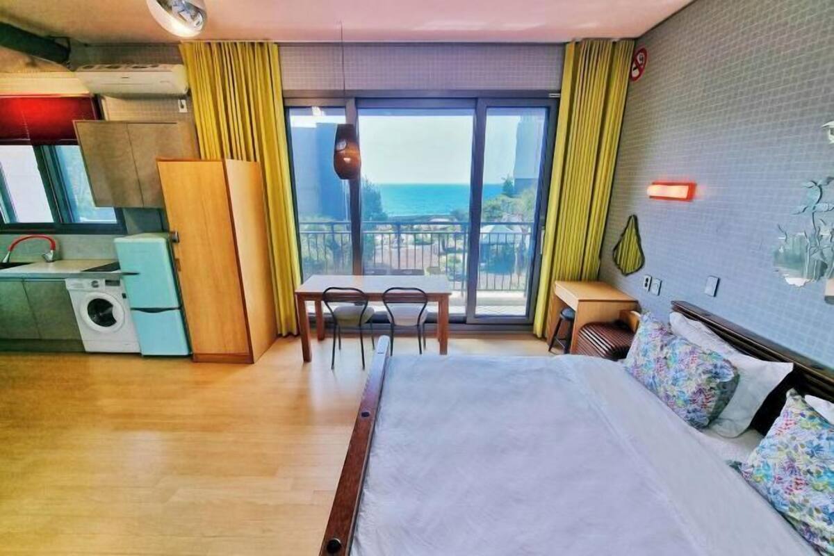 A hotel room with a bed, a small kitchenette, a dining area, and a balcony with a view.