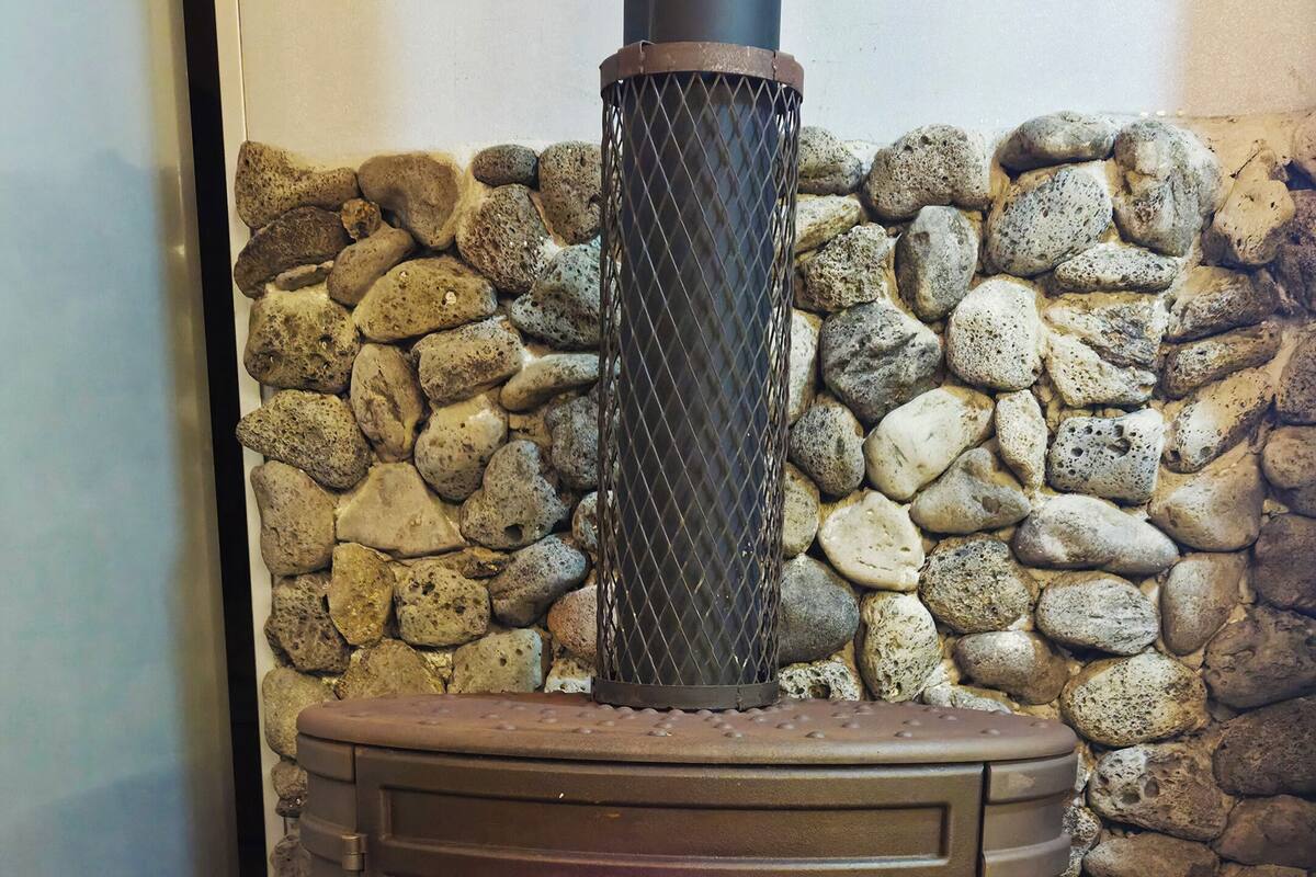 A wood-burning stove with a stone wall backdrop, logs on the floor, and a metal grate on top.