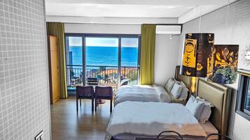 Habitación de hotel con dos camas, un balcón con vistas al mar y un amplio ventanal con cortinas.