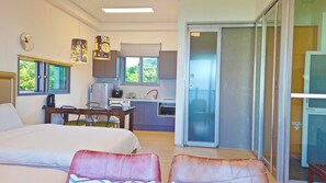 A hotel room with a bed, a desk, a chair, a kitchenette, and a sliding glass door leading to a balcony. - OROJEJU (Seogwipo)