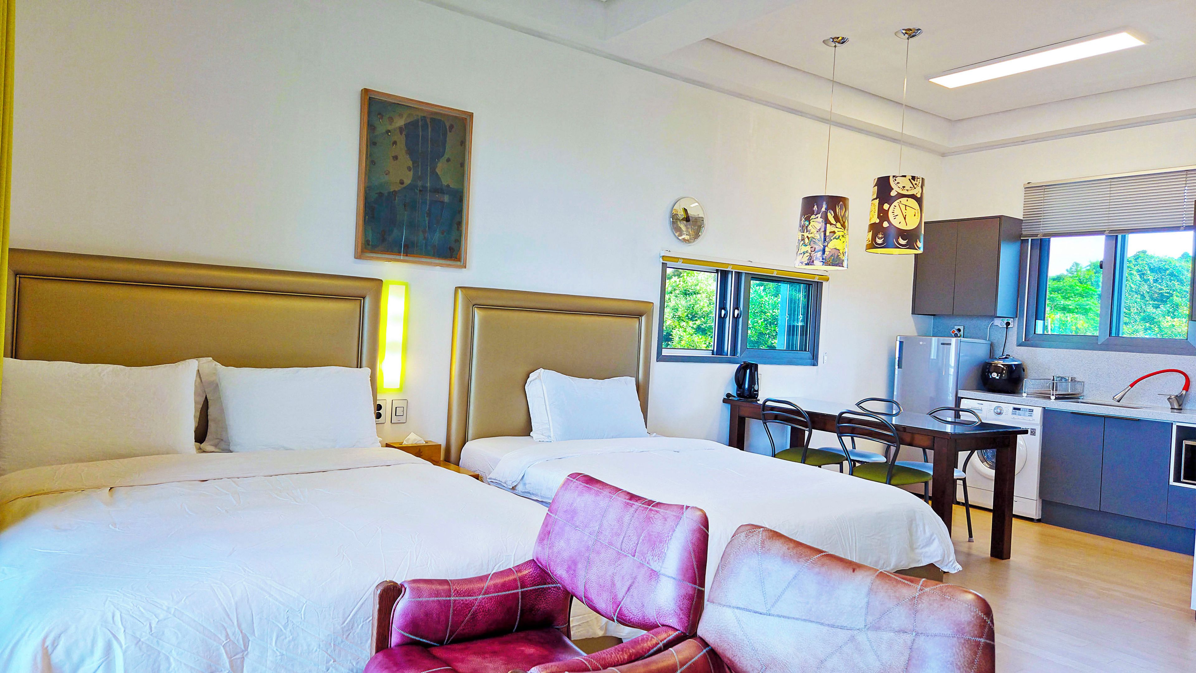 A hotel room with two beds, a desk with a chair, a window with a view, and a kitchen area.