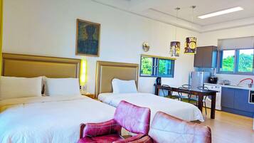 A hotel room with two beds, a desk with a chair, a window with a view, and a kitchen area.