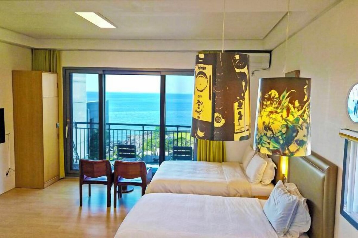Habitación de hotel con dos camas, un balcón con vista al mar y una mesa con sillas.