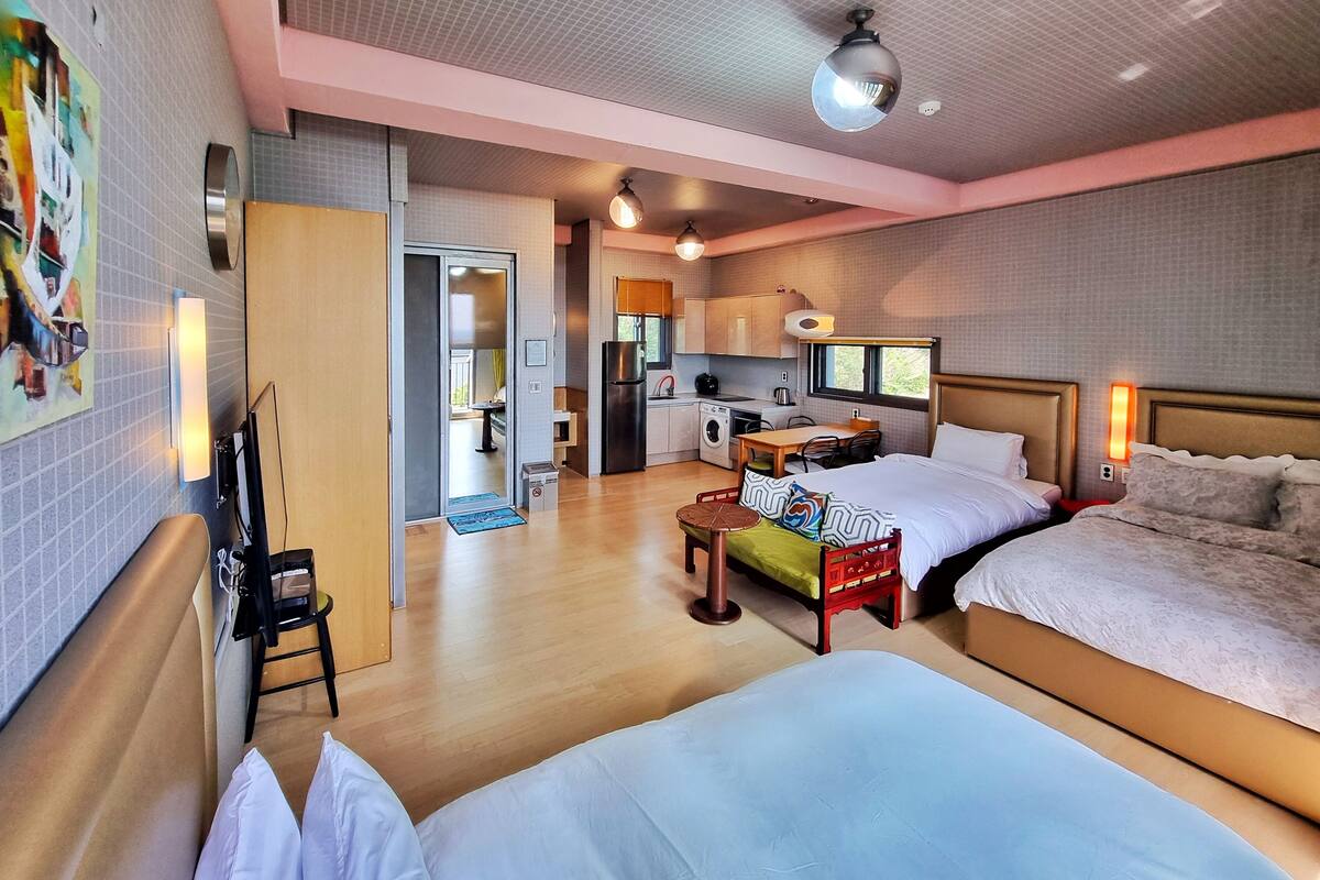 A hotel room with two beds, a kitchenette, a dining area, and a bathroom.