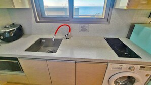 Una cocina con un lavabo, un grifo rojo, un horno empotrado y una lavadora.