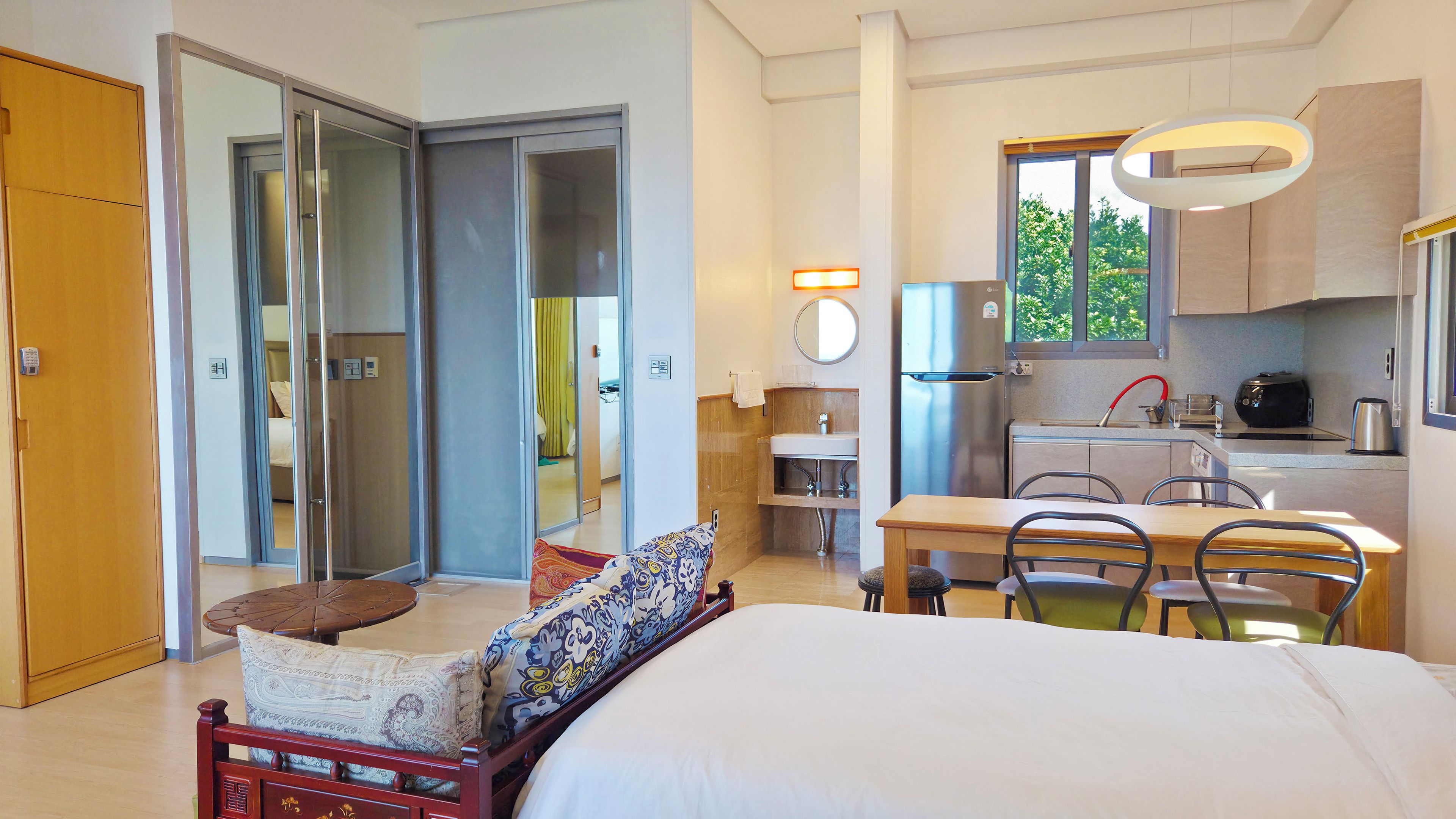 Une chambre d’hôtel comprenant un lit, une petite table, des chaises, un coin cuisine et une porte coulissante donnant sur une autre pièce.