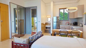 Habitación de hotel con cama, una mesita, sillas, zona de cocina y puerta corredera que da a otra habitación.