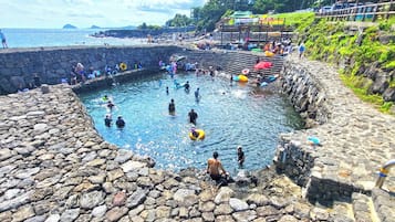 Una piscina de piedra rodeada por un muro de piedra, con gente nadando y de pie cerca.