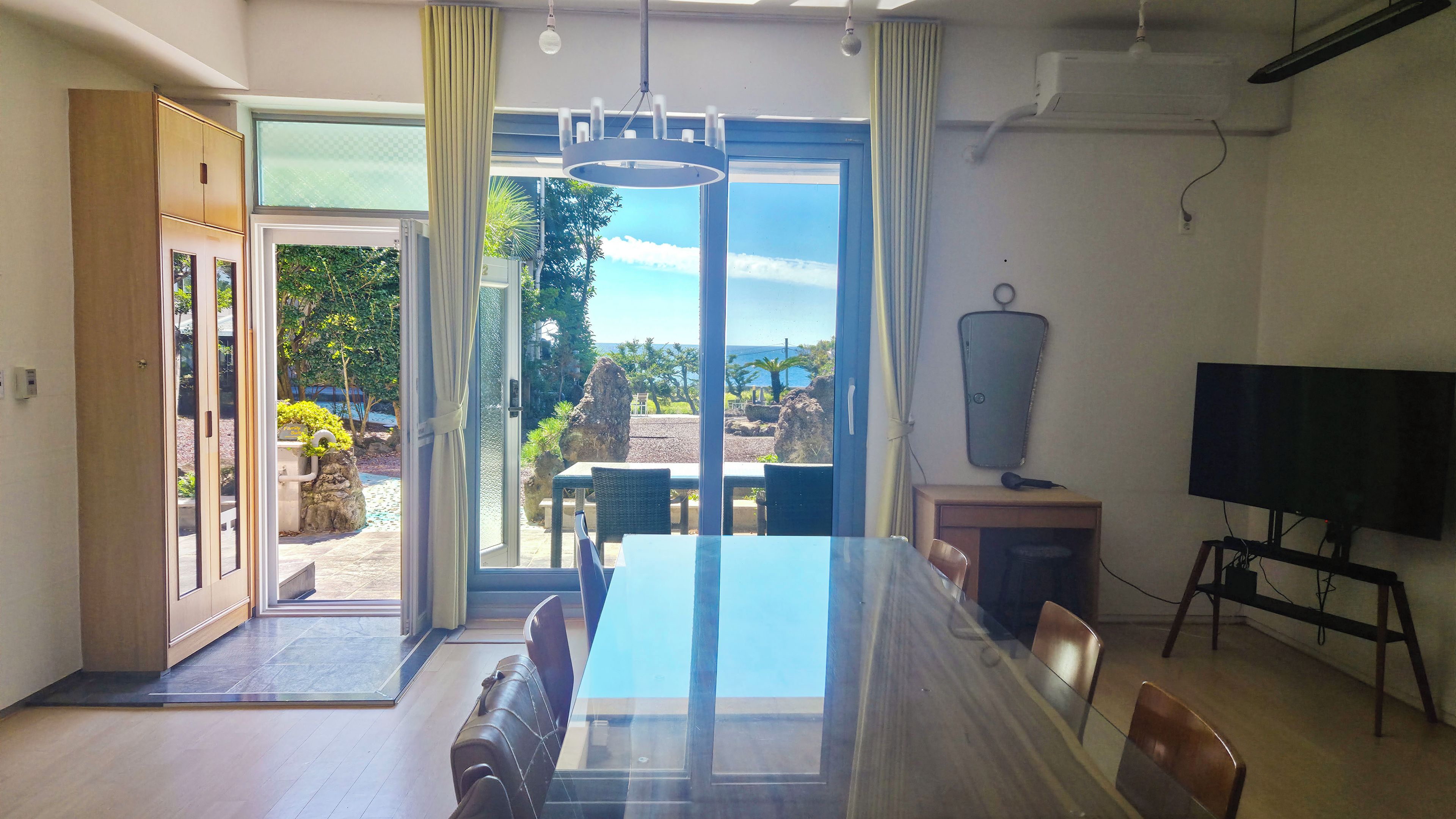 A modern dining area with a glass table and chairs, a television, and a view of the outdoors.