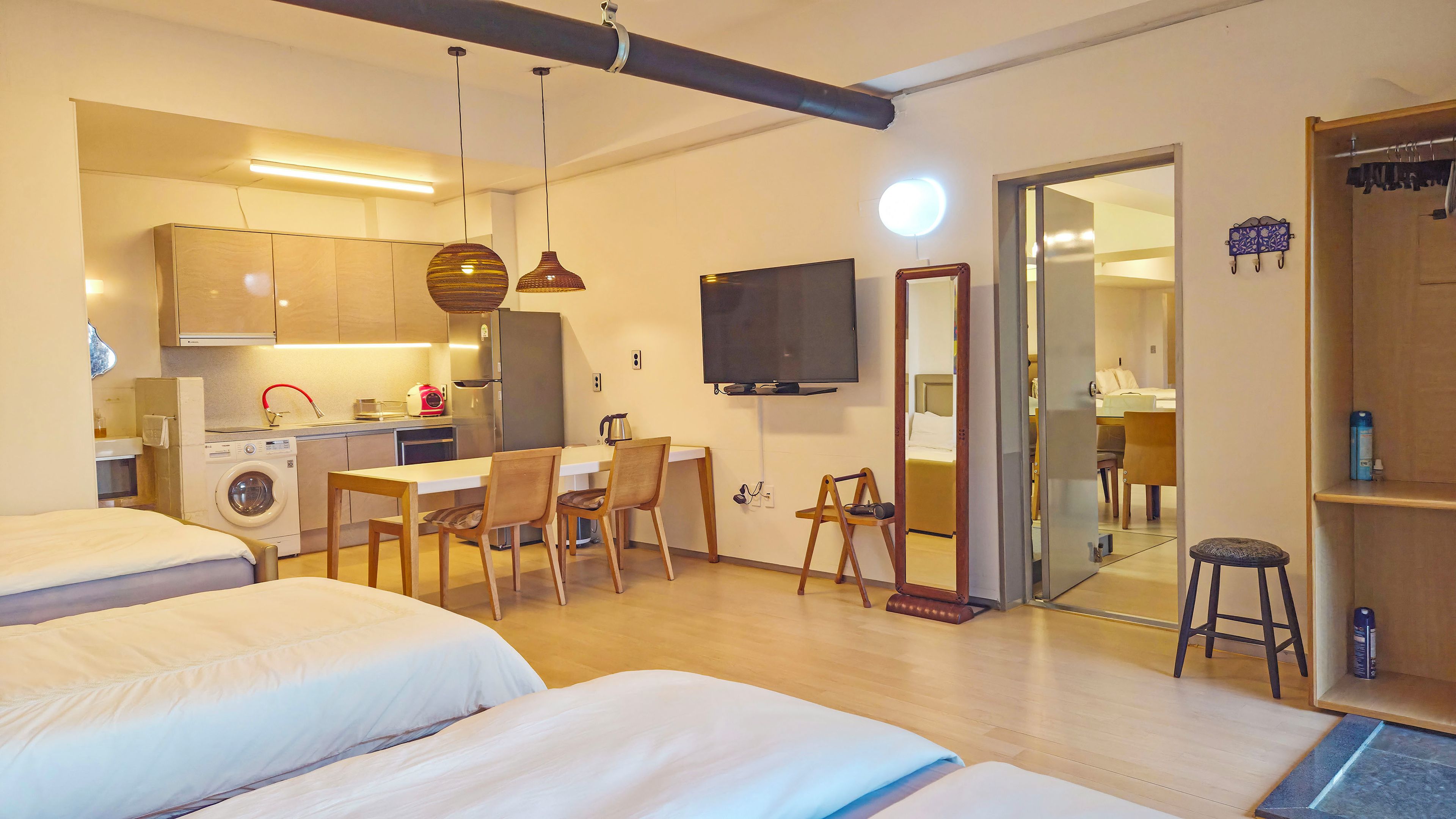 Habitación de hotel con kitchenette, zona de comedor, televisor y un espejo grande.