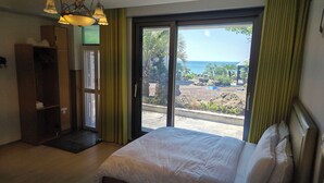 Habitación de hotel con cama, armario y puerta que da a un balcón con vista al mar.