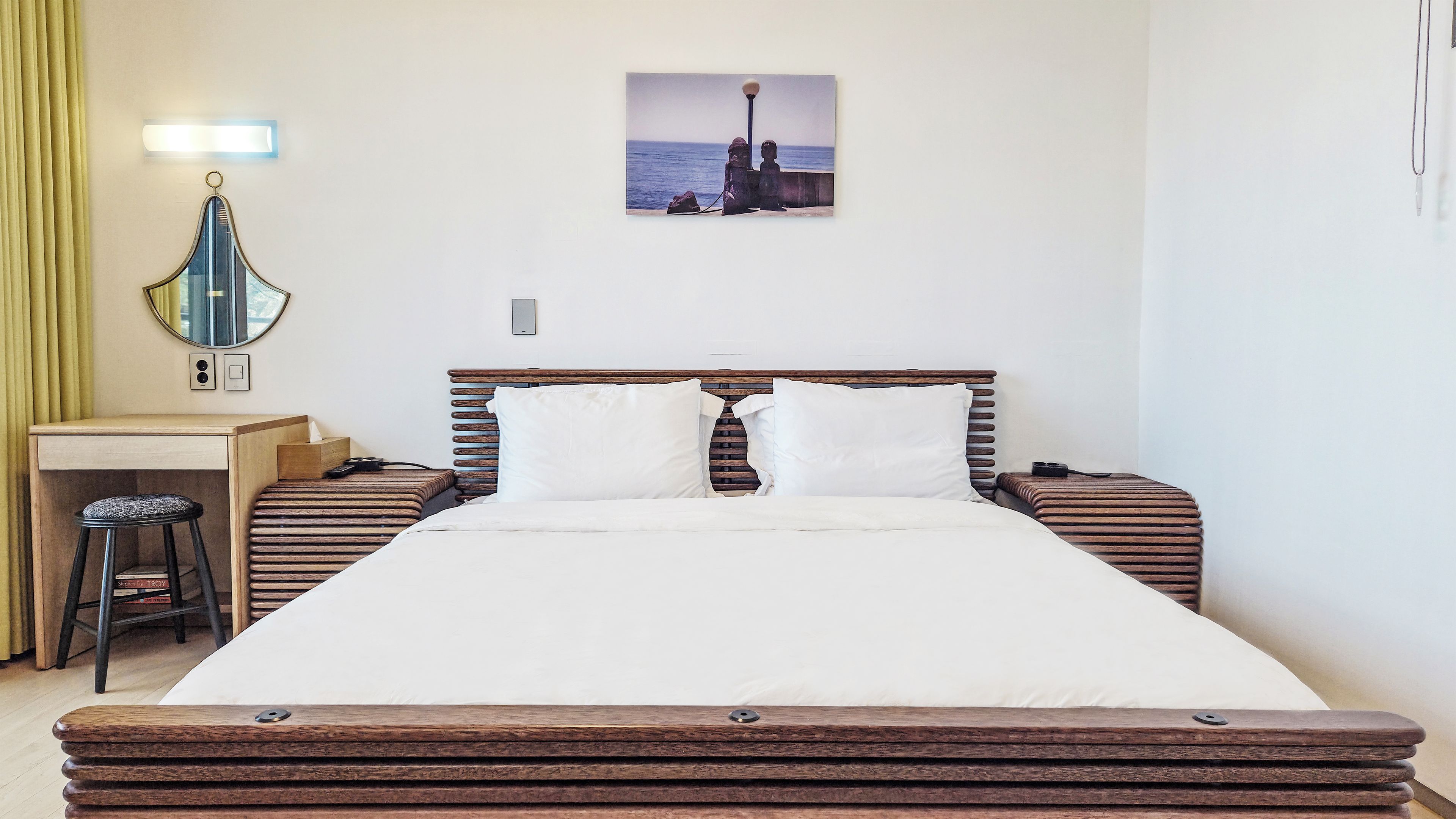 A hotel room with a bed, bedside tables, a desk, a chair, a mirror, and a picture on the wall.