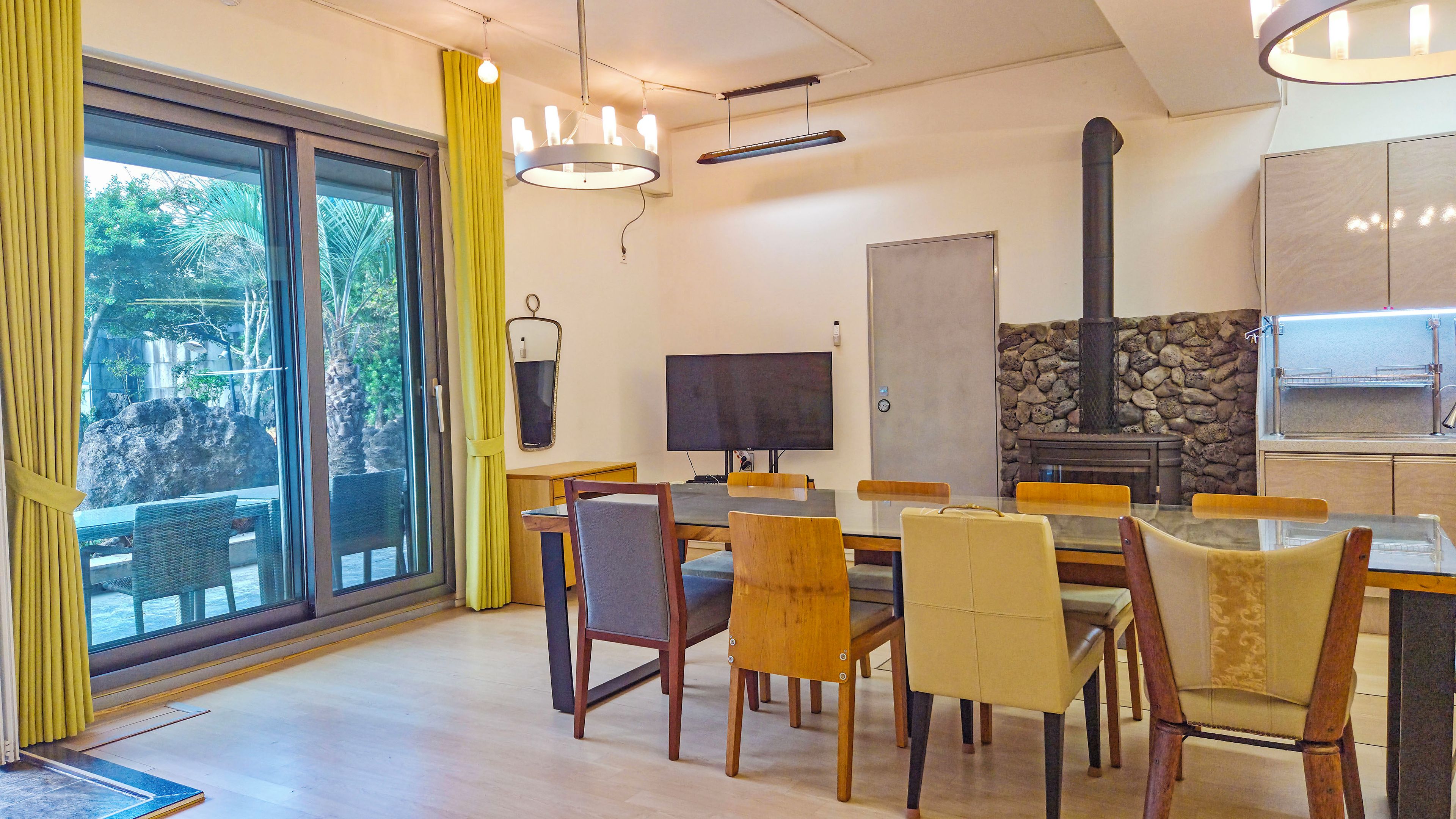 A dining area with a large table, chairs, a television, and a stone fireplace.