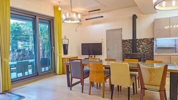 A dining area with a large table, chairs, a television, and a stone fireplace.