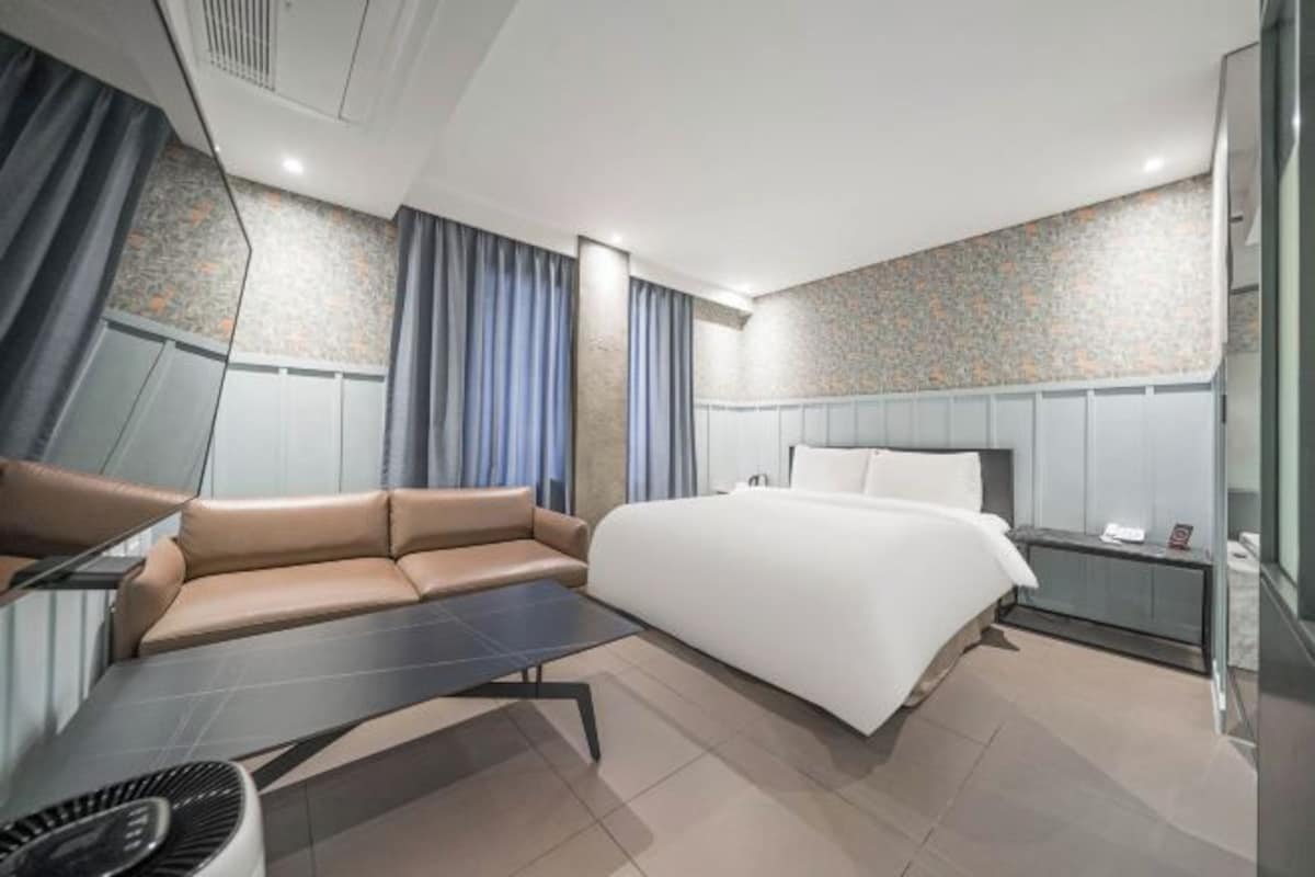 A modern hotel room with a bed, a sofa, a small table, and a mirror.