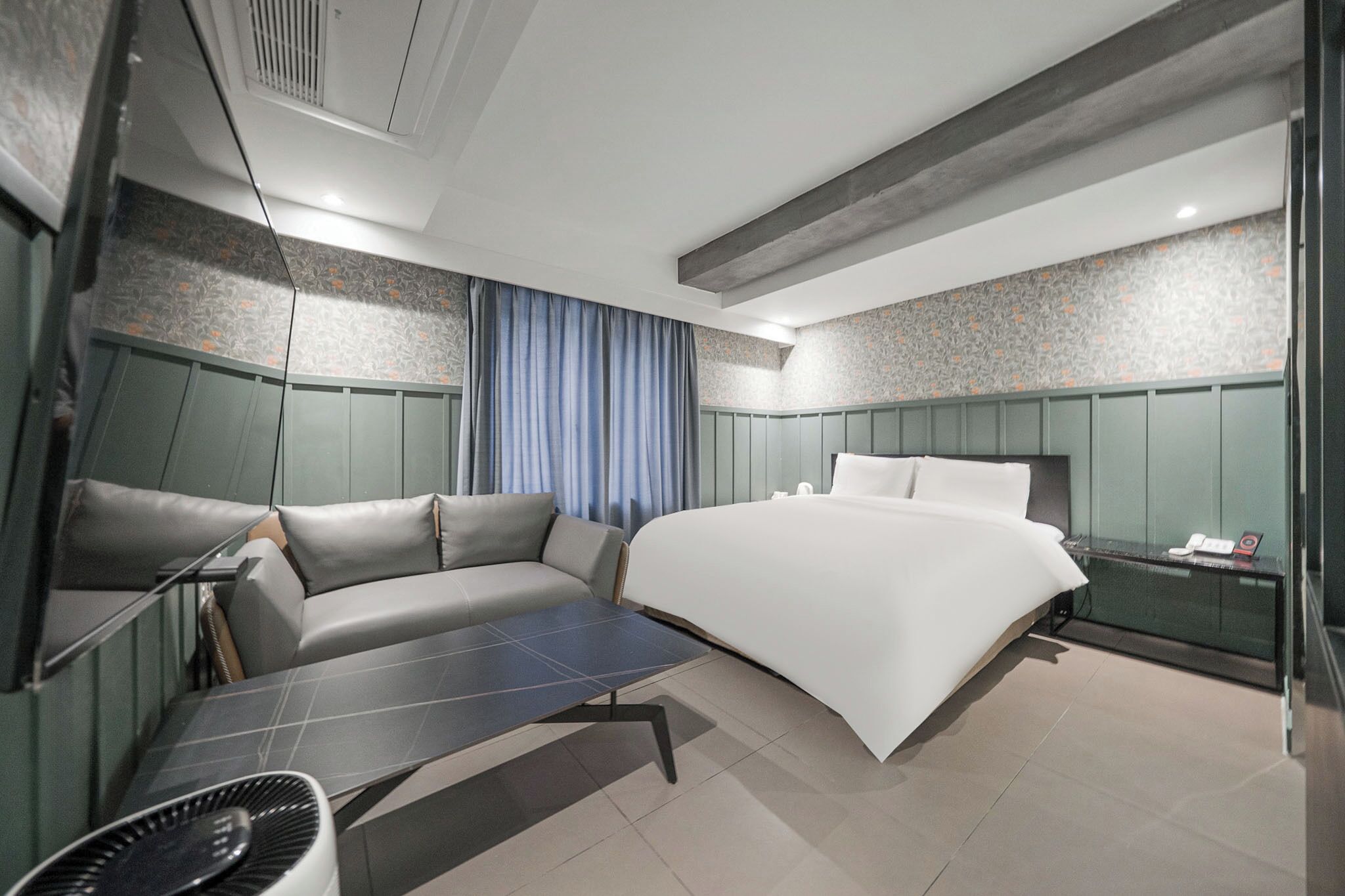A modern hotel room with a bed, a sofa, a small table, and a nightstand.